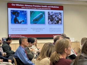 Image of a slide showing biomedical data science research graphics from Sylvia Plevritis' research. An audience listens to the presentation.